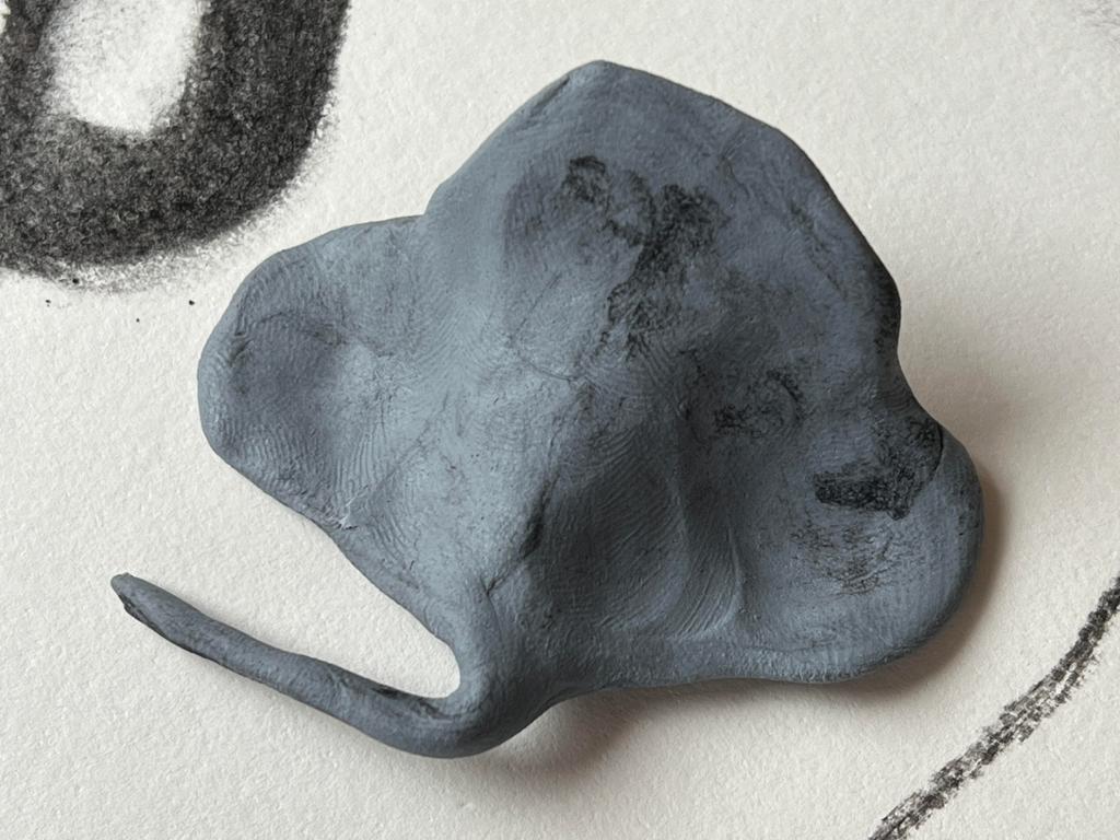 Et grått viskelær formet som noe som likner en elefant med ører og snabel, ligger på et papir som har spor etter kullstift. Foto.