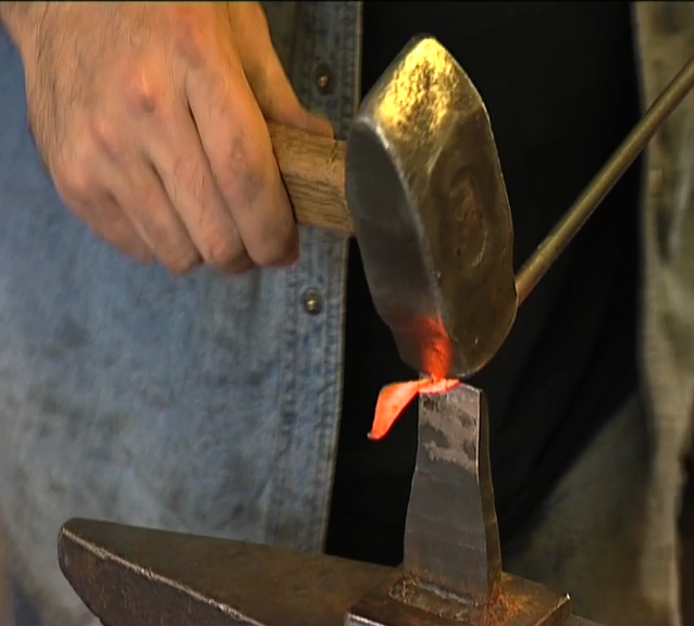 Hånd med hammer som jobber med glødende metall. Foto.