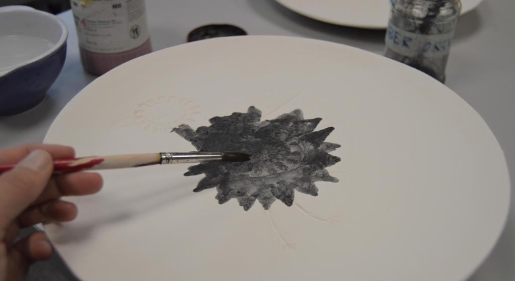 Oksid blandet med vann blir penslet på et hvitt keramikkfat. Foto.