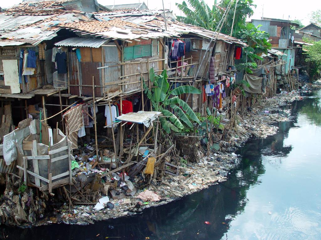 Et slumområde i Jakarta. Husa ligger tett og ser skrøpelige ut, og det er høyt, urent vann tett på bebyggelsen. Foto.