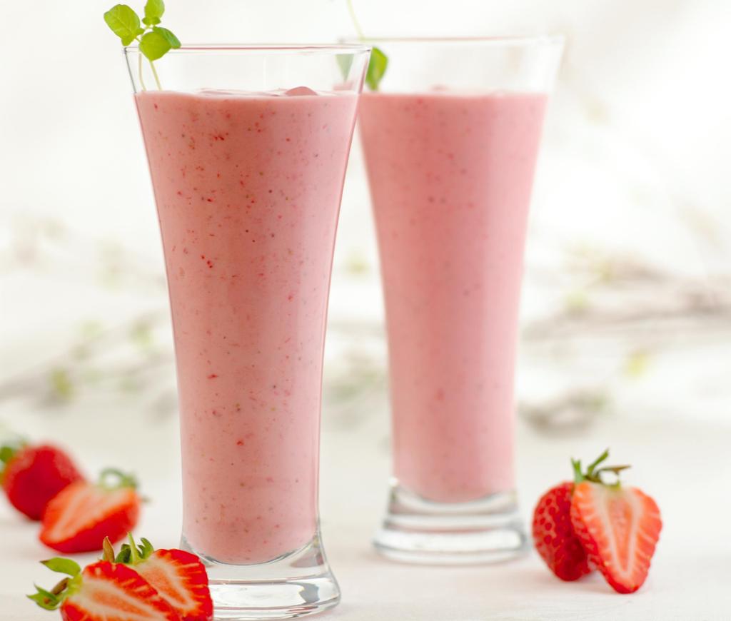 To høye glass fylt med jordbær-smoothie. Pyntet med urter og med oppkuttede jordbær rundt. Foto.