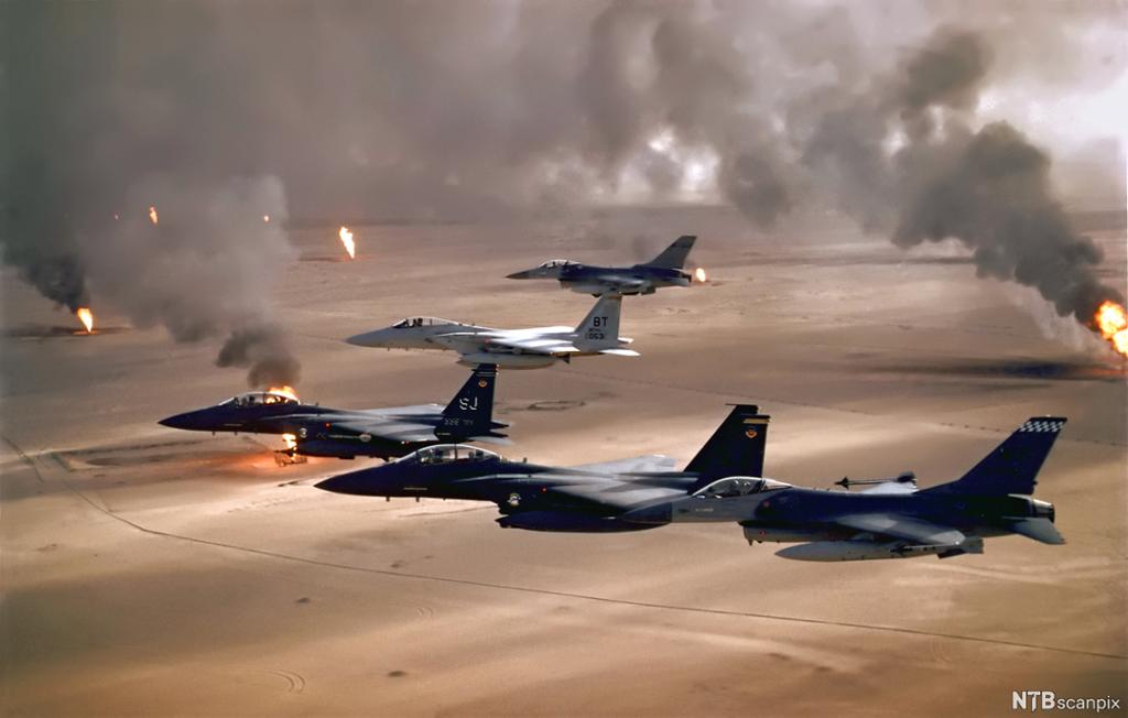 Jagerfly over brennende oljebrønner i et ørkenlandskap. Foto.