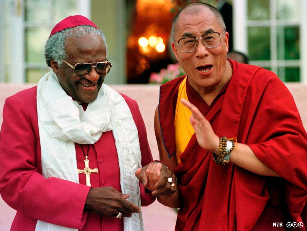 Biskop og buddhistisk munk smiler og holder hender. Foto.