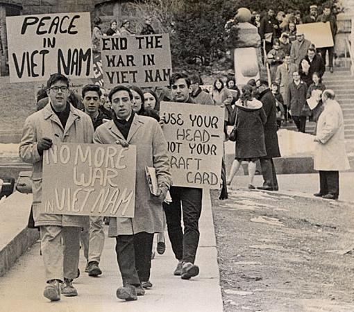 Ei stor gruppe unge menneske går i demonstrasjonstog. Dei held opp plakatar mot Vietnamkrigen og for fred. Svart-kvitt foto. 
