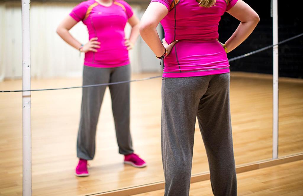 Ei jente i treningsdrakt ser på seg sjølv i spegelen. Foto.
