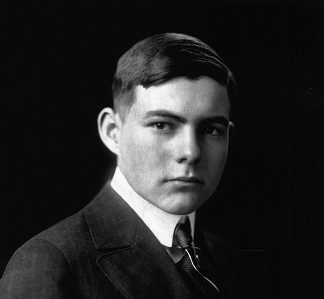 Photo: Portrait of Ernest Hemingway. We see a young, dark-haired man. He is wearing a suit and tie. 