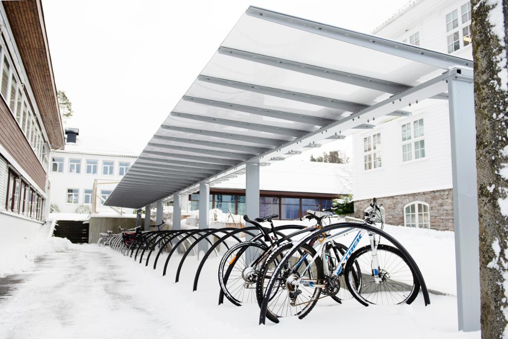 Et sykkelstativ med tak med noen sykler parkert under. Det er vinter og snø på bakken. Foto. 