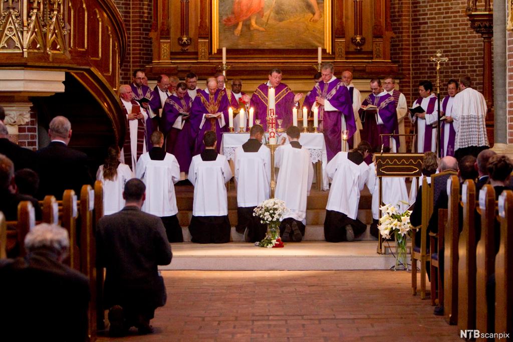 Biskoper og prester med lilla og hvite kapper ved alteret i en katolsk kirke. Foto.