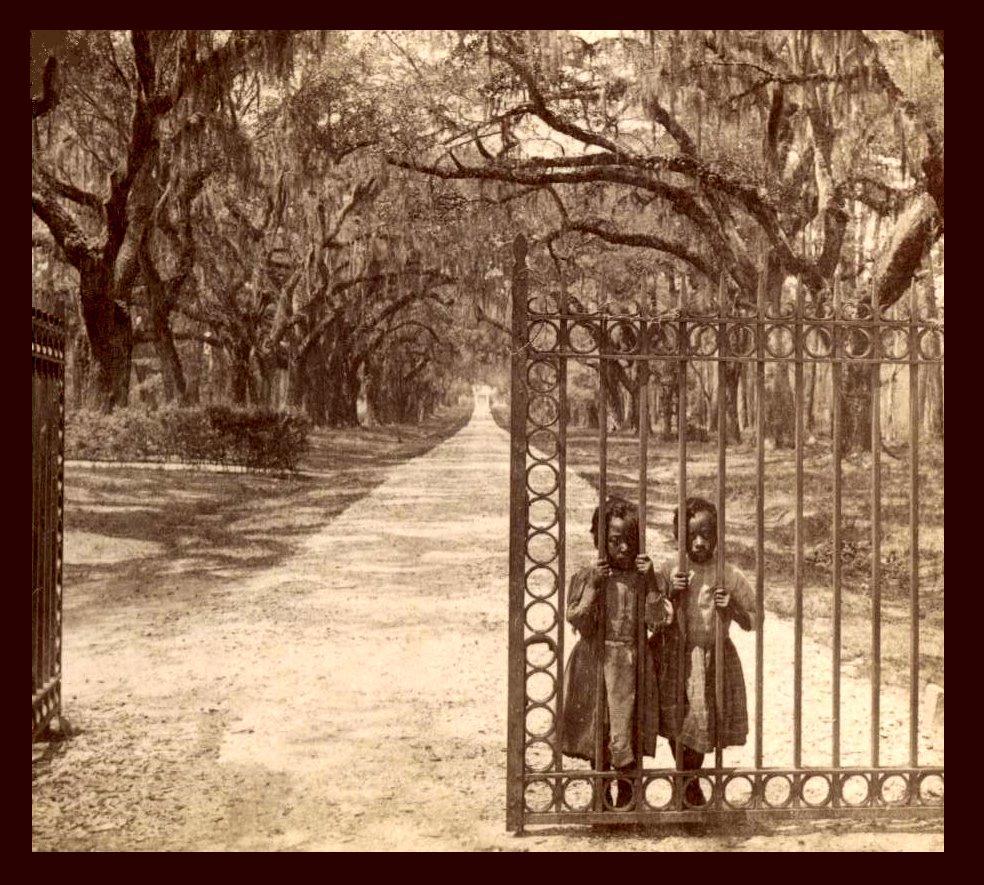 Two girls standing behind a barred gate. Photo.