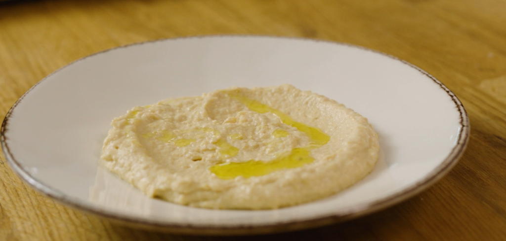 Hummus anrettet på en hvit tallerken med olje over. Foto.