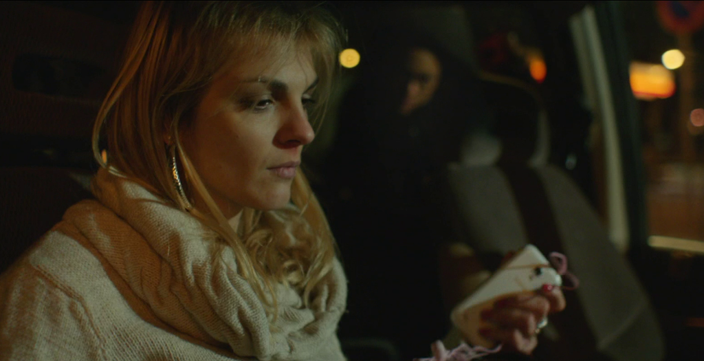 En ung kvinne sitter i passasjersetet i en bil. Hun holder en mobil i hånda. Foto.