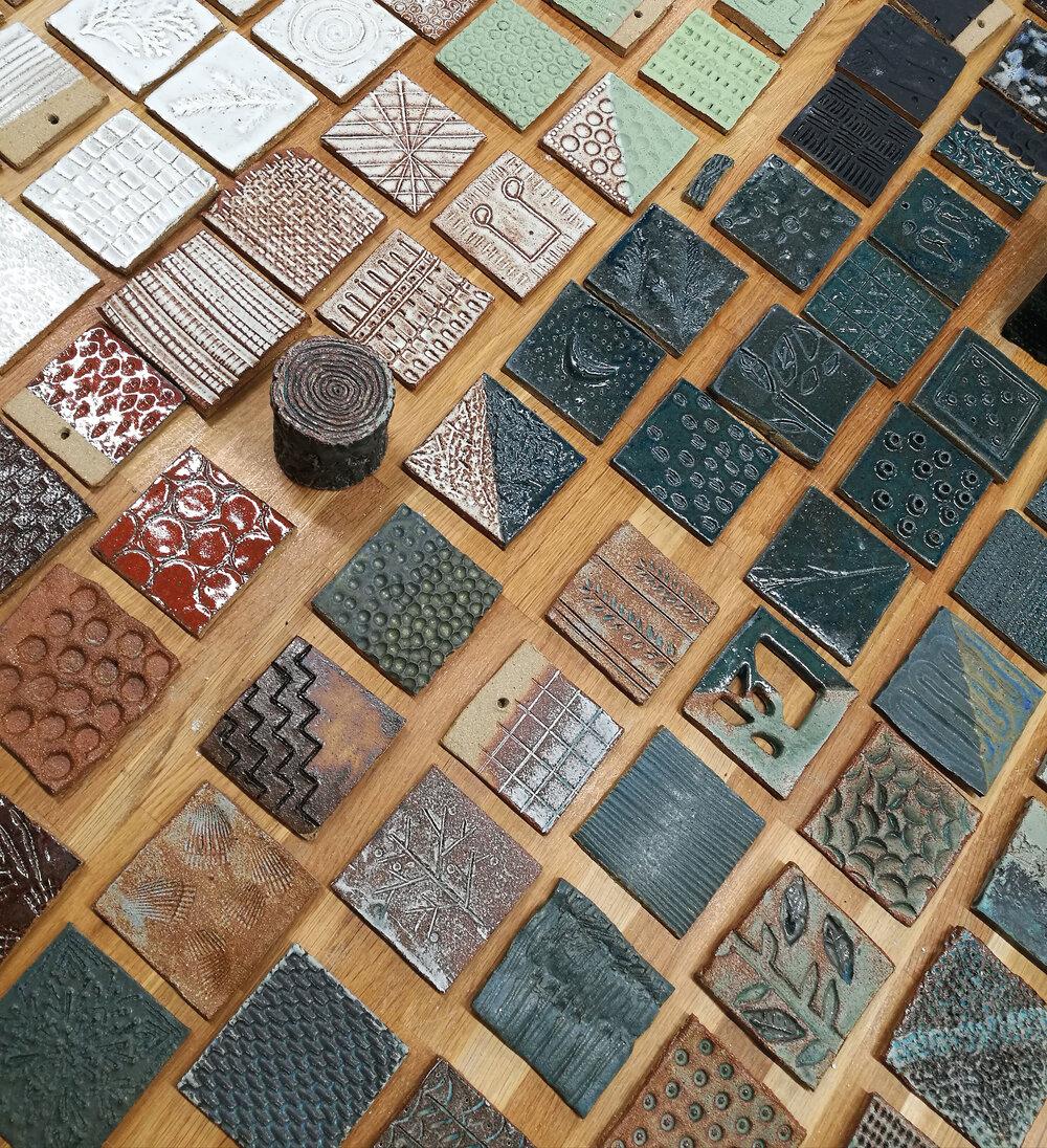 Keramikkfliser med ulike teksturer som ligger på et bord. Foto.
