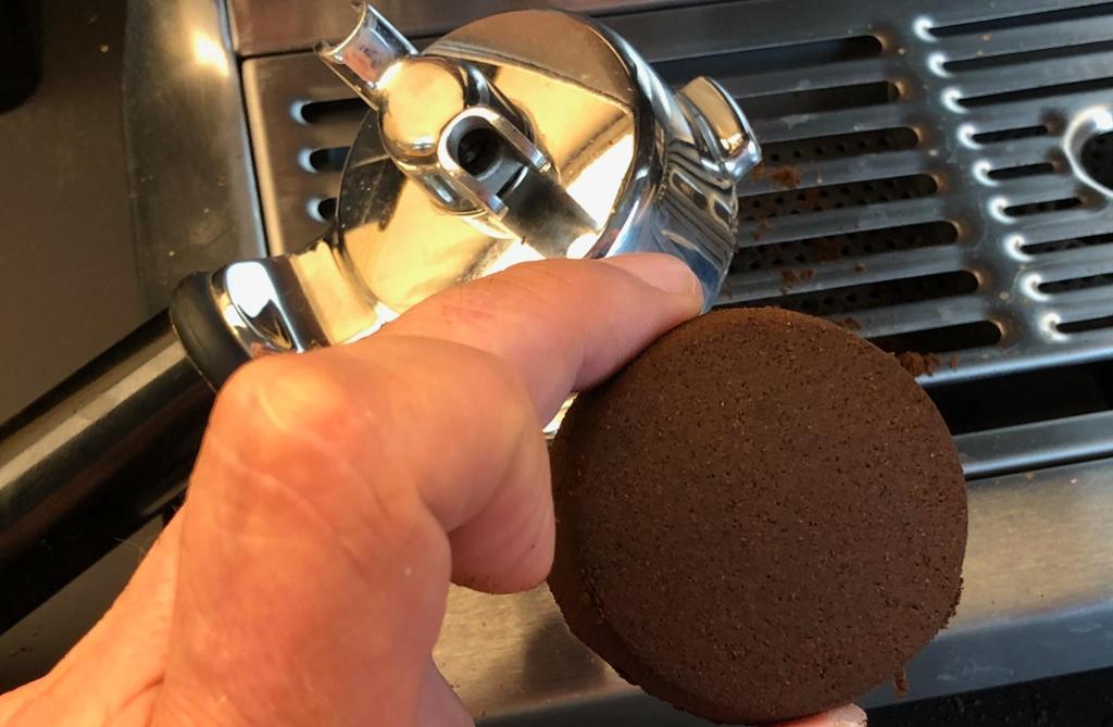 En hånd holder en kaffekake fra en espressomaskin. Foto.