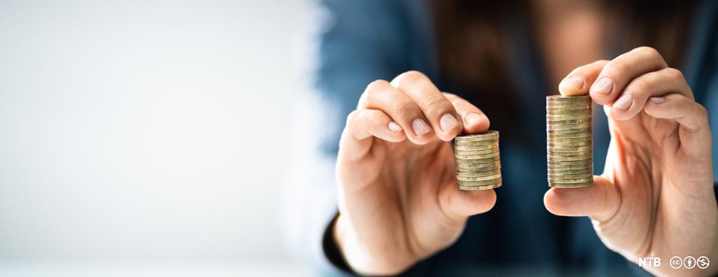 A woman is holding up two stacks of coins, one larger than the other. Photo.