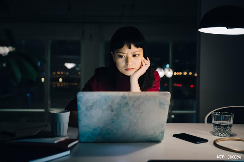 Kvinne som sitter foran en laptop og ser på skjermen med et kritisk blikk. Foto.