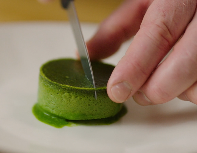 En liten, grønn, lav spinatsylinder skjæres i to med en liten kniv. Foto.