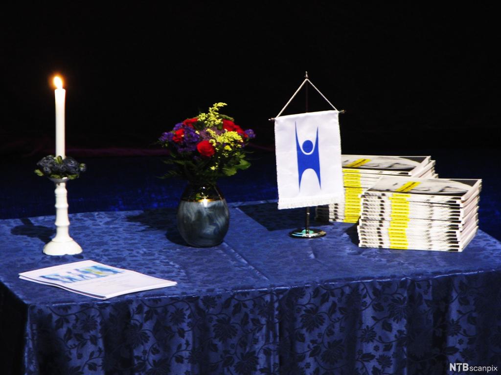 Bord med stearinlys, blomar, bunkar med bøker og eit banner med logoen til Human-etisk forbund. Foto.