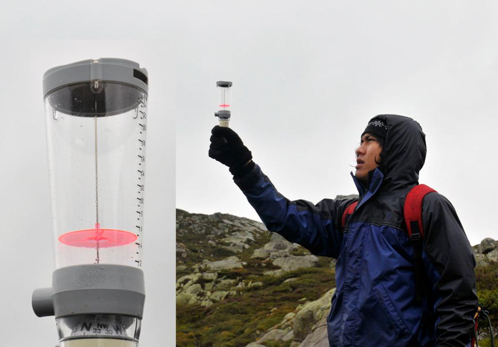 Ein elev kledd i regntøy held oppe ein vindmålar i eit fjellandskap. I eit utsnitt til venstre ser vi eit nærbilete av vindmålaren, som er ein plastsylinder med grått lok. Foto