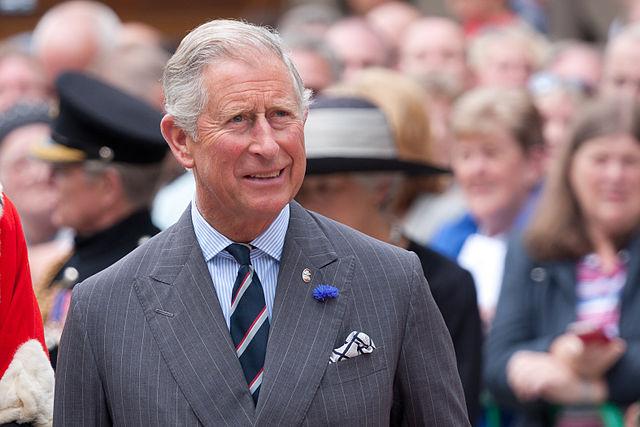 The Prince of Wales, today King Charles III. He's wearing a grey suit. There are many people in the back wanting a glimps of the king. 