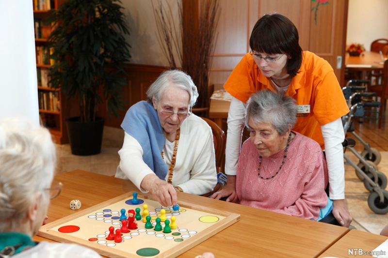 Aktivitør og tre gamle damer spiller ludo. Foto. 