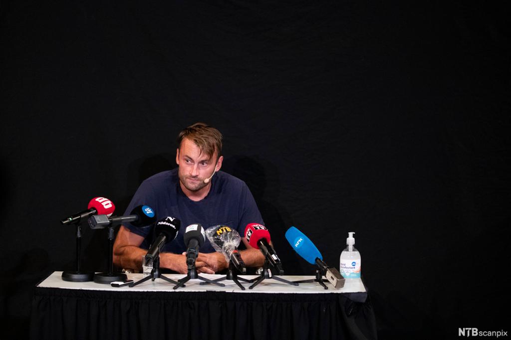 Petter Northug sitter ved et bord fullt av mikrofoner. Han ser alvorlig ut. Foto.