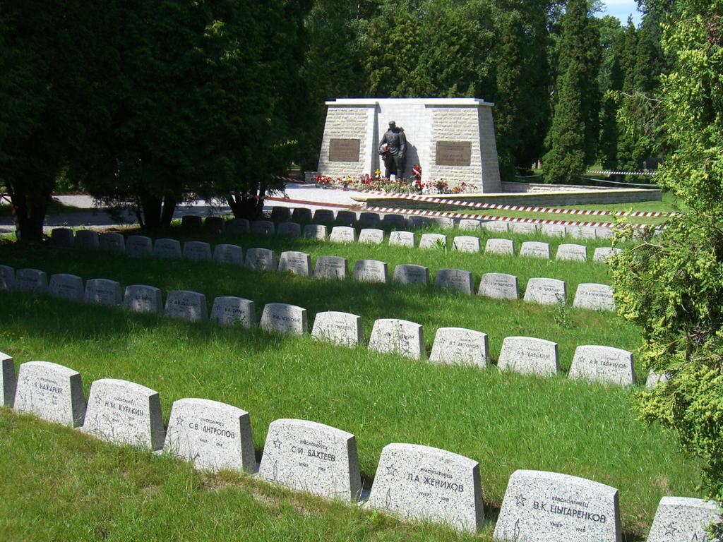 Kirkegård med hvite graver og en statue av en soldat i bakgrunnen. Foto.