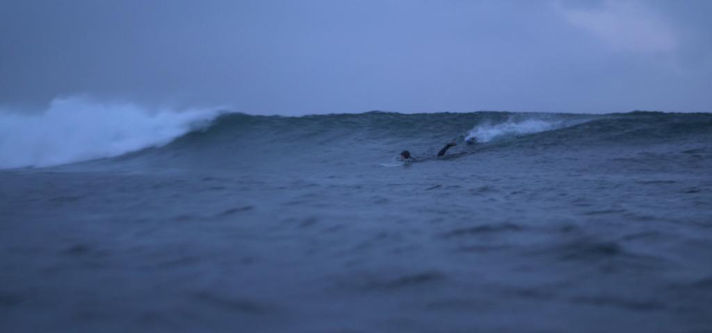 Foto av en surfer som ligger på magen i en bølge. 
