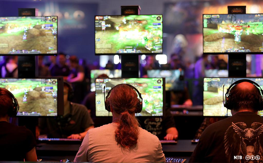 Mennesker med headset foran ei rekke skjermer som de spiller spillet World of Warcraft på. Foto. 