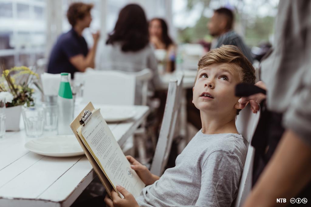 Foto av en gutt som holder et menykart og snakker med servitøren på en restaurant.