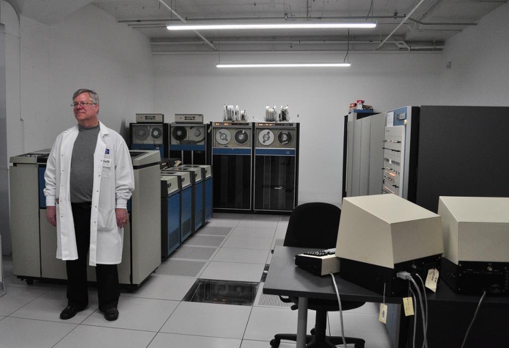 Et stort hvitt rom med flere skap med tapemaskiner og datautstyr. En mann står ved siden av. Foto.