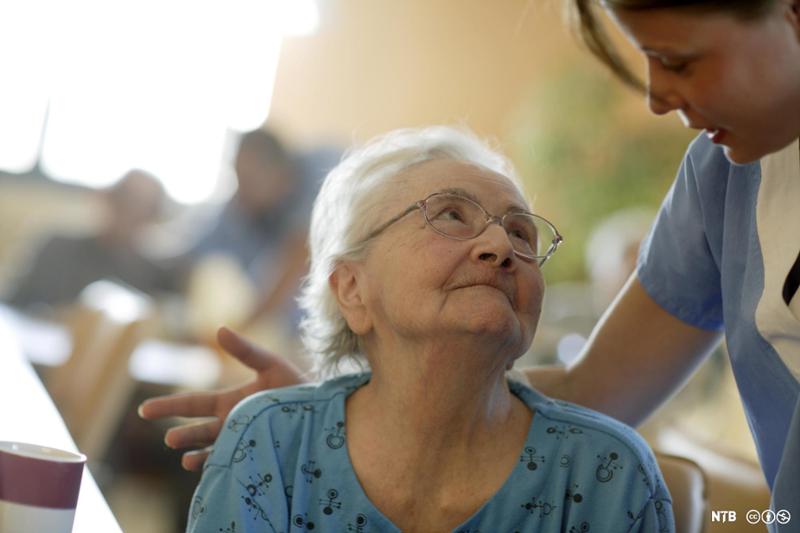 Eldre dame på sykehjem ser med takknemlighet på helsefagarbeider. Foto.