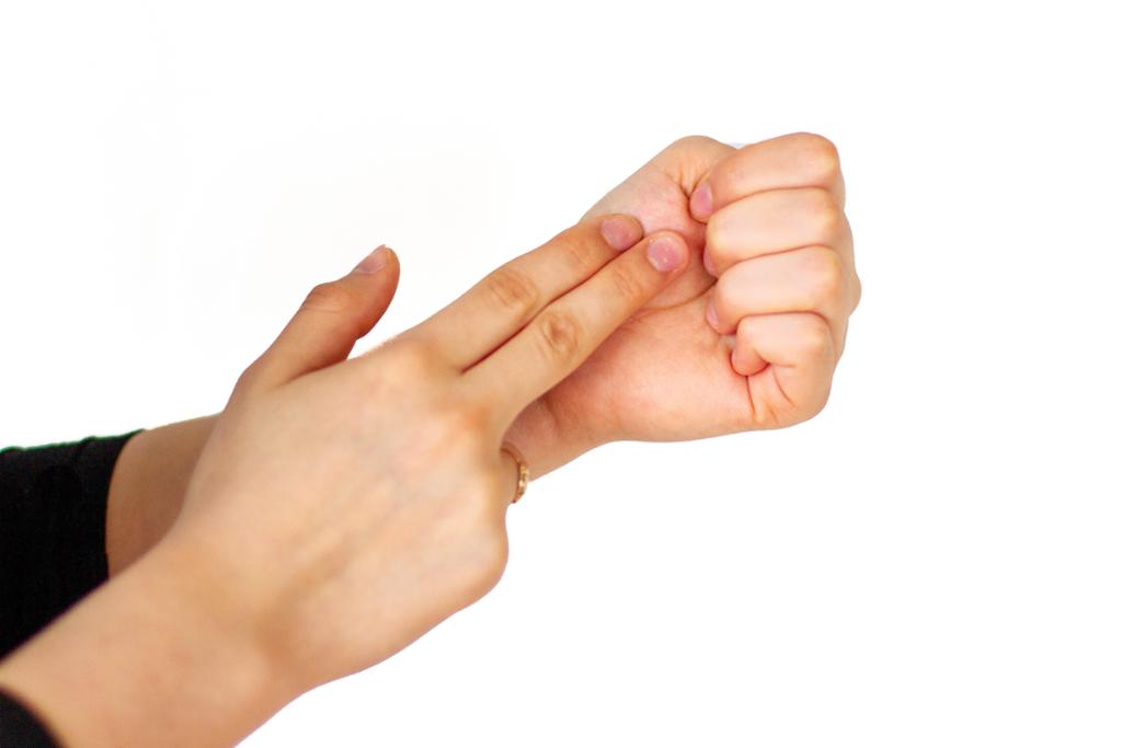 To fingre som trykker lett på den delen av hånda som knytter sammen tommelen og håndflaten, på en knyttet neve. Foto.