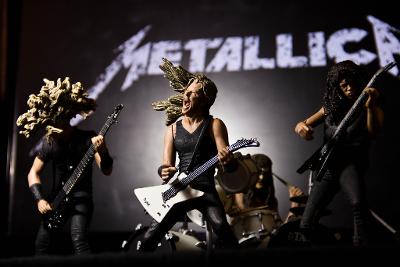 Metallband i scenelys som dukkeversjon med instrumenter, på veggen bak står det Metallica. Foto.