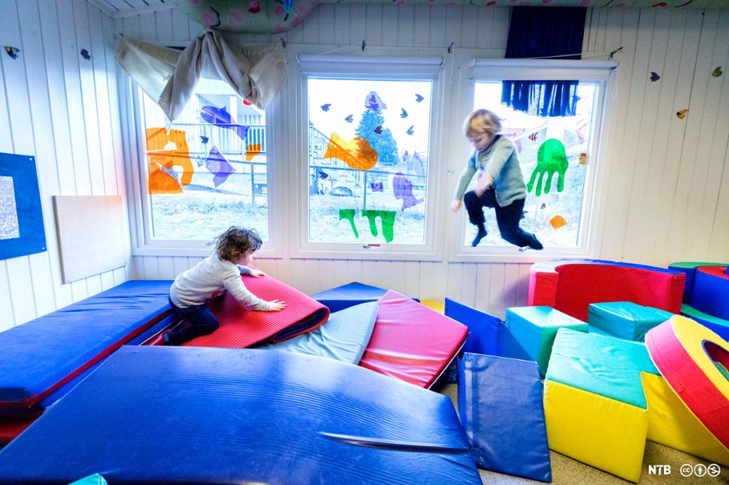 Et rom som er fullt av store plastbelagte puter og madrasser som barn kan leke med. To barn leker i putehaugen, det ene er midt i et høyt hopp over putene. Foto.