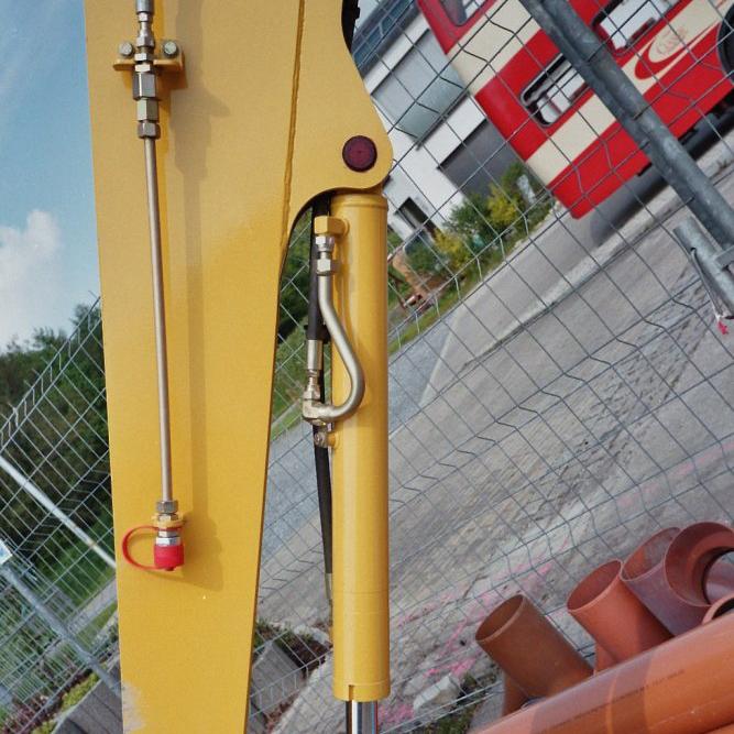 Hydraulikksylinder med koblinger på gul løftearm. Foto.