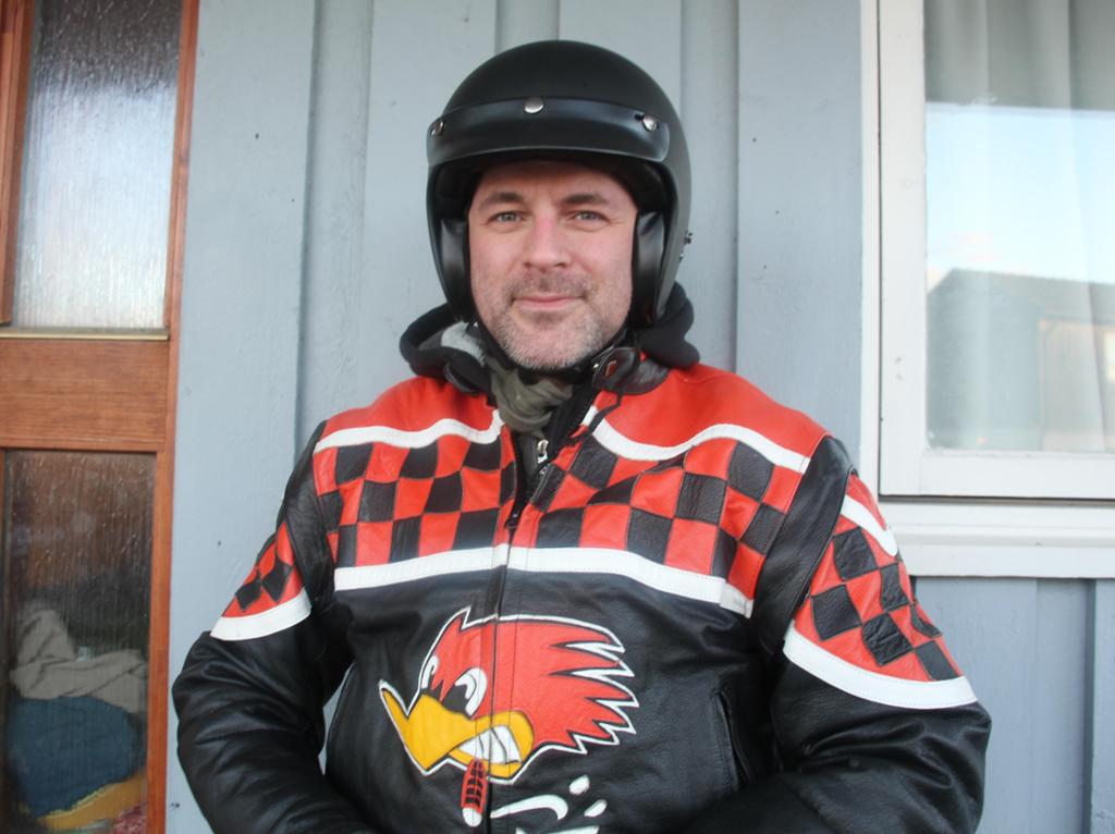 Foto av ein mann med fargerik motorsykkeljakke og svart halvhjelm.
