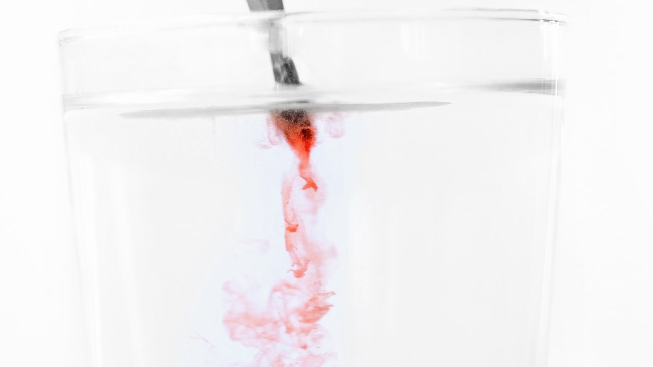 Rennende rød maling fra pensel ned i et glass med vann. Foto. 