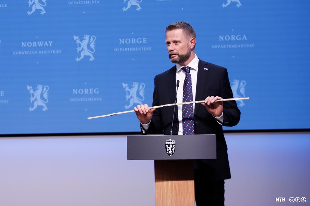 Statsråd Bent Høie viser fram meterstokken under en pressekonferanse om koronasituasjonen. Foto. 