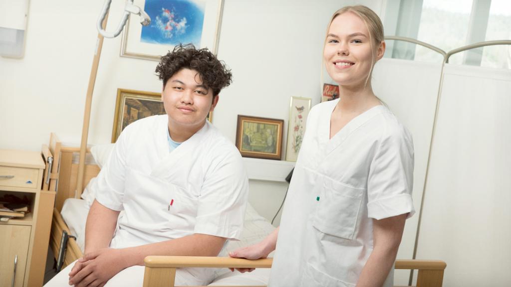 To smilende helsefagarbeidere ved ei pasientseng. Foto.
