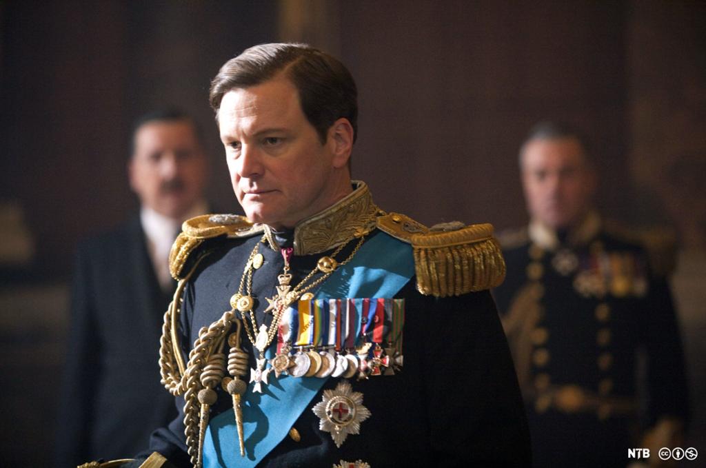 Colin Firth as George VI in the film The King's Speech. We see a middle-aged man with dark hair. He is dressed in a full dress uniform and looks very somber.  Photo. 