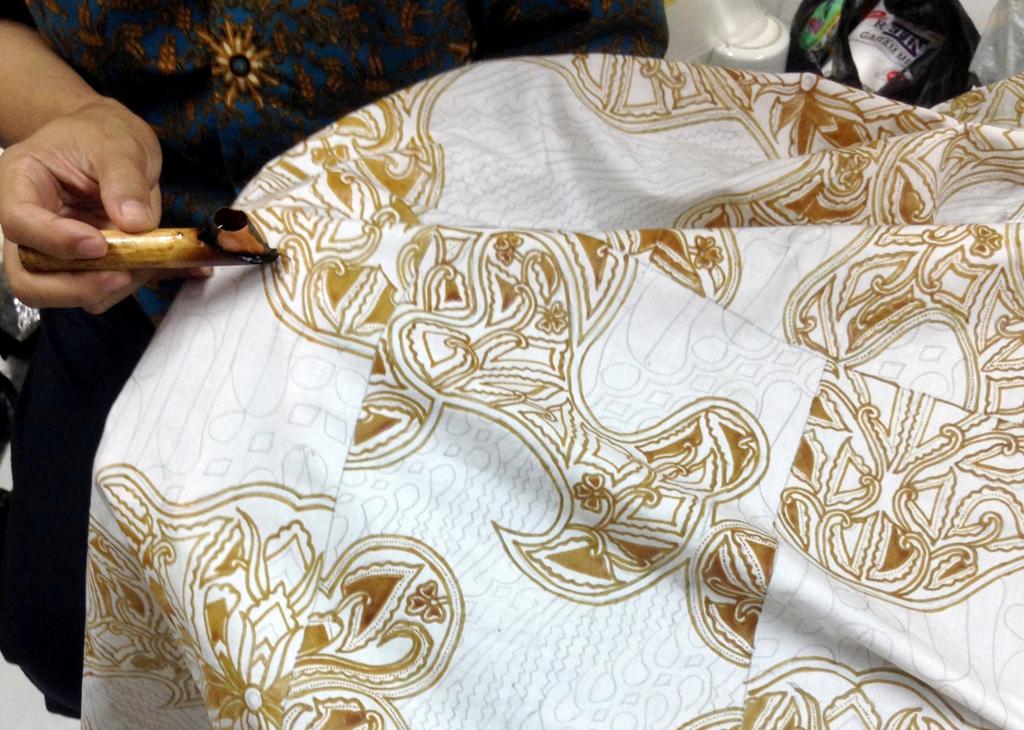 En liten metallkanne brukes til å påføre flytende voks, slik at det skaper et mønster i tekstilet. Foto.