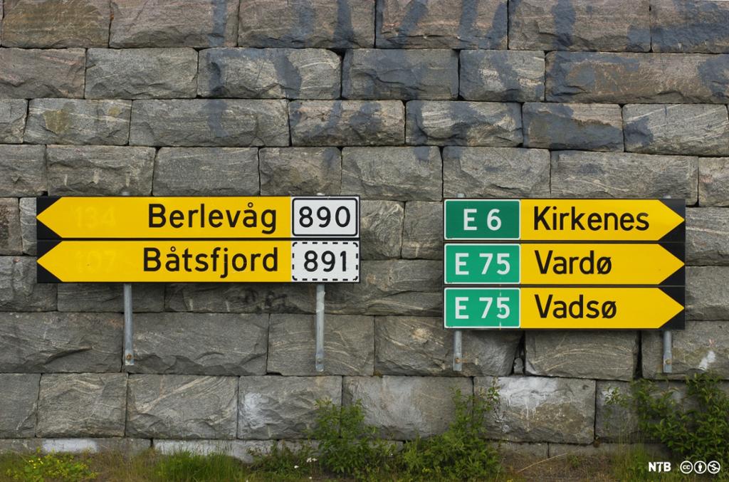 Fem veiskilt på en steinvegg. To skilt peker mot venstre. På disse skilta står stedsnavna Berlevåg og Båtsfjord. Tre skilt peker mot høyre. På disse skilta står stedsnavna Kirkenes, Vardø og Vadsø. Foto.