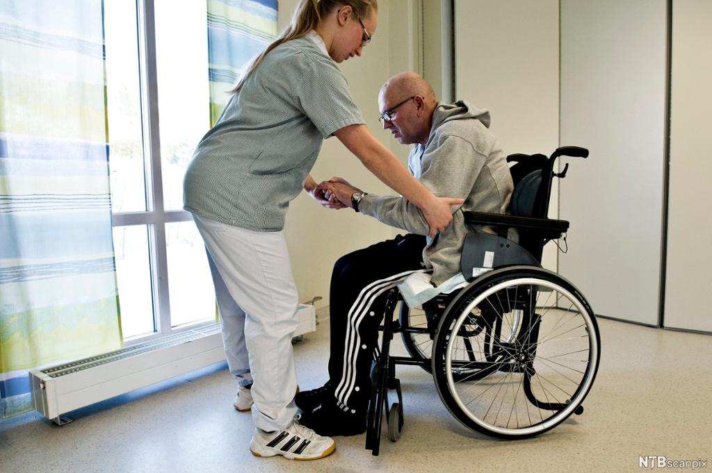 Kvinnelig helsefagarbeider hjelper en mann i rullestol. Foto.