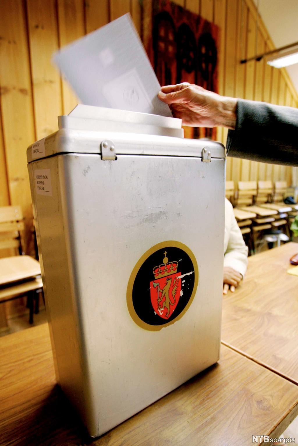 Person avgir stemme ved valg, stemmeseddel og valgurne. Foto.