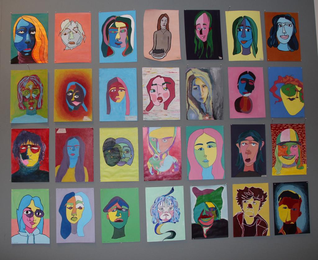 Ein vegg med mange fargerike sjølvportrett laga med blindkontur. Foto.