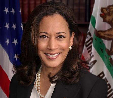 Photo of Kamala Harris standing in front of the flag of the United States of America and the state flag of California.