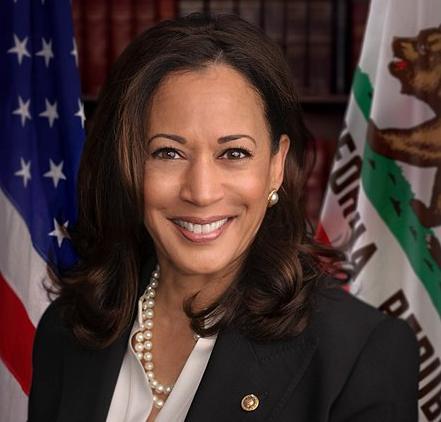 Photo of Kamala Harris standing in front of the flag of the United States of America and the state flag of California.