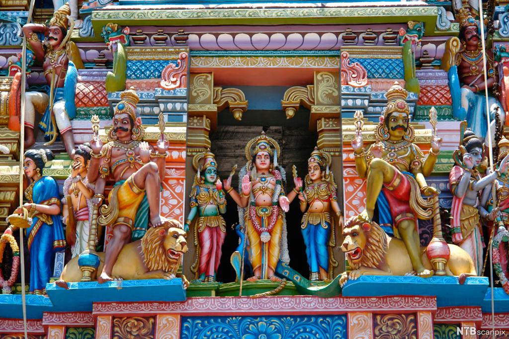 Fargerike gudefigurer framfor et hinduistisk tempel. Foto.