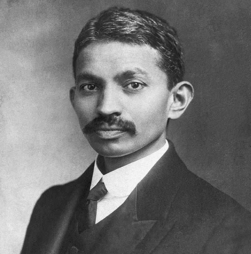 Photo: We see a portrait of a young Indian man in a suit. He has a very formal suit with vest and tie. He has a large moustache. He has short, dark hair.