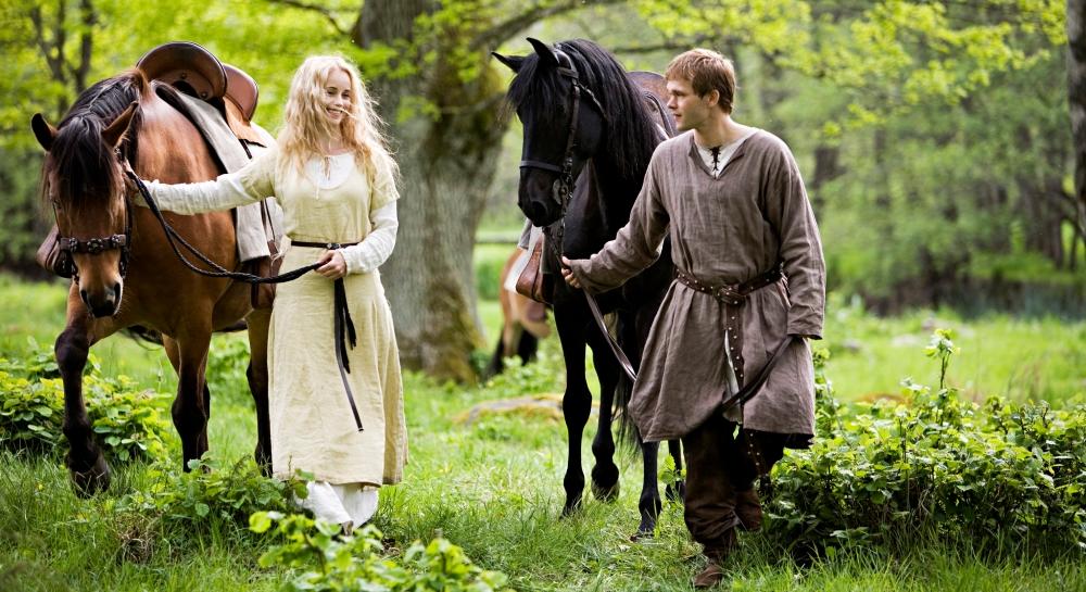Et ungt par i middelalderklær går gjennom skogen med hestene sine. Foto.